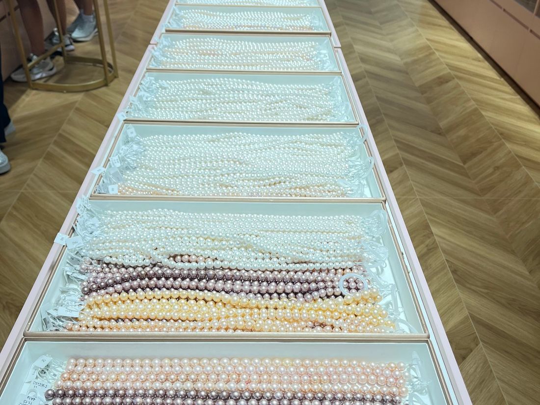 A long showroom counter with trays of white, cream and coloured freshwater pearl strands